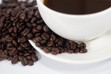 coffee beans heap with white cup and saucer . black and brown color seeds background . close up nutrition textured