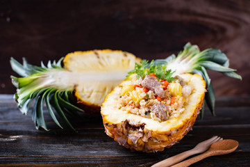 Fried rice with pork in half pineapple fruit on wooden background, Thai cuisine