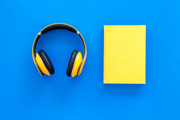 Books online concept, audiobooks. Spend leasure time reading and listening music. Headphones near hardback book with empty cover on blue background top view copy space