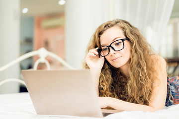 Happy young woman is sitting relax playing laptop on bed at her bedroom.woman working on laptop while sitting at his working place in her home