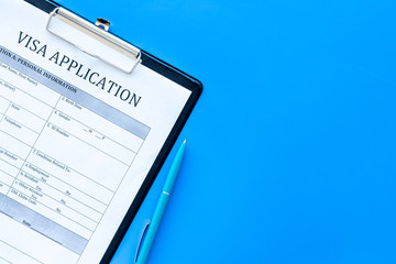 Visa prosessing. Registration of visas. Visa application form and pen on blue background top view...