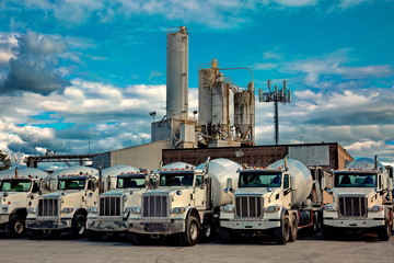 A range of cement mixer trucks  in a parking lot of a cement factory.