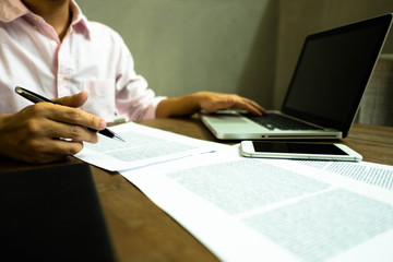 Fototapeta premium Businessman working at office with laptop and documents on the table, Businessman holding pens and papers taking notes in documents on the table.