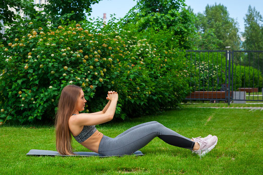 Beautiful thin woman sportswoman doing the exercise, swinging the press on a yoga mat before training on a green lawn in the park on a summer day