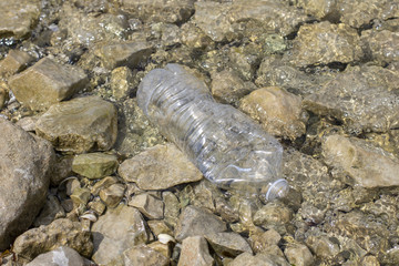 Empty plastic water bottle littering lake shore