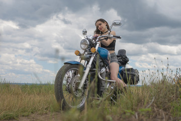 Fototapeta na wymiar brunette biker on a motorcycle in black leather jacket. lavender field against the sky with clouds. slow motion