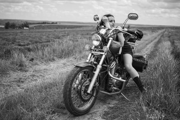 Fototapeta na wymiar brunette biker on a motorcycle in black leather jacket. lavender field against the sky with clouds. slow motion