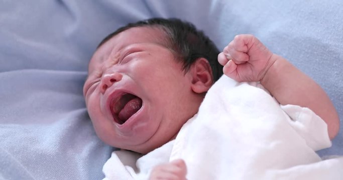 New born baby crying on bed