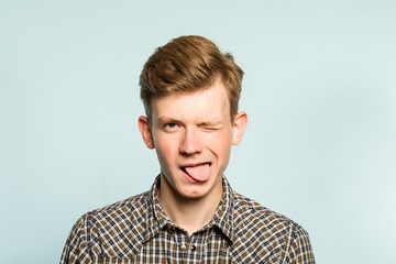 joyful playful man sticking tongue out. happy joyous emotion. portrait of a young guy on light...