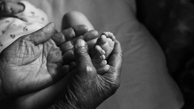 Great-grandmother touching little baby foot, black and white shot, the concept of a family and a new life into a selective focus