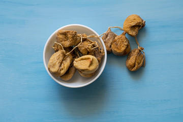 Dried figs in a white bowl on a blue table. Dried fruit.
