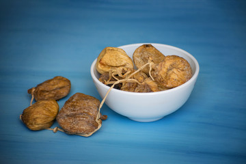 Dried figs in a white bowl on a blue table. Dried fruit.