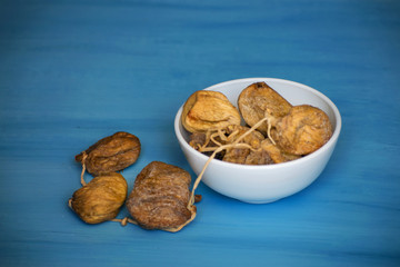 Dried figs in a white bowl on a blue table. Dried fruit.
