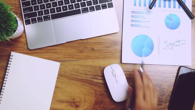 Business people use pen to point graphs to analyze company data and statistics from the chart.