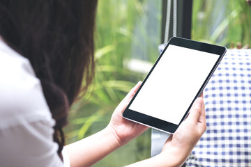 Mockup image of woman holding black tablet pc with blank white desktop screen and green nature background