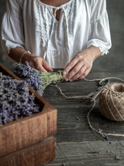 Female florist holding bunch of lavender tied by twine. Working table with wooden box of lavender, ...