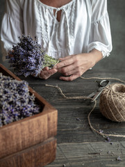Female florist holding bunch of lavender tied by twine. Working table with wooden box of lavender,...