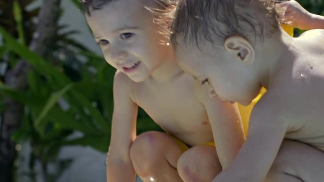 Two cute little boys playing with small water fountain in swimming pool at hot summer day