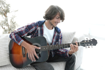 Handsome man playing on the guitar on the couch at home