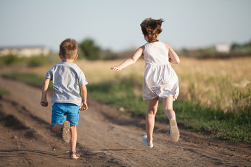 Children run in the field on the road. A boy and a girl are playing active games.