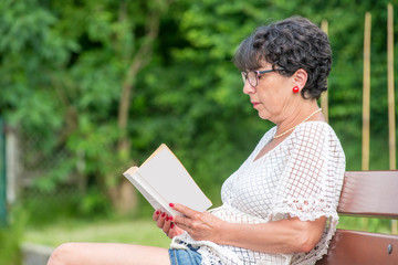beautiful senior woman reading book in the garden