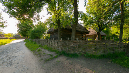 a wooden house with a reed roof near a wicker tin under high trees