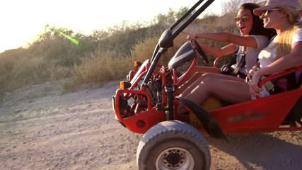 Young girls go on dune buggy on dirt road enjoying extreme rest. Riding along sandy road on beach buggy. Girls driving dune buggy. Extreme trip on earth road. Extreme vacation ride