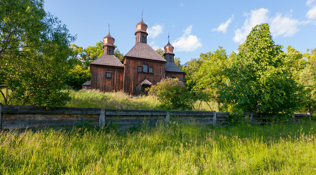 An old wooden church with three shining domes overgrown with tall grass. As in the film Viy