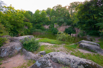 Fototapeta na wymiar A small green transparent lake on a background near stone boulders and green vegetation
