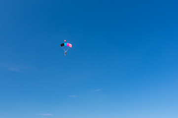 Fototapeta na wymiar Blue sky and colorful parachute carrying lonely human to the earth