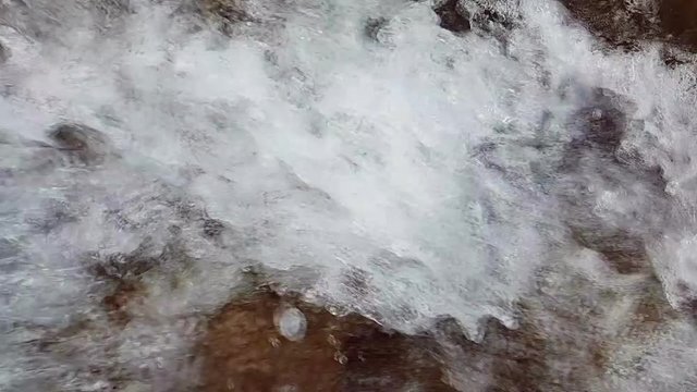 Background or texture. Slow motion of a small mountain waterfall. 240fps. The mountain stream falls down on stones in a bottom.