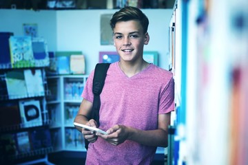 Portrait of happy schoolboy holding digital tablet in library