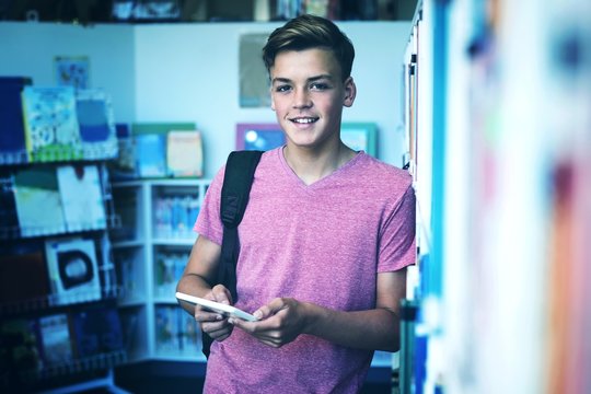 Portrait of happy schoolboy holding digital tablet in library