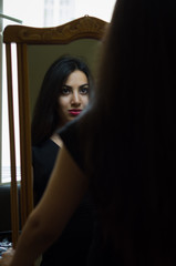 Young charming brunette girl looks at her reflection in the mirror