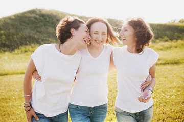 Family portrait of a positive mother hugs her daughters in white T-shirts and jeans against the...
