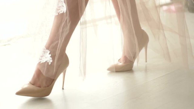 Close-up of a girl in high heels and a long translucent dress is on the catwalk, slow motion. Underwear. The bride in the negligee in the boudoir.
