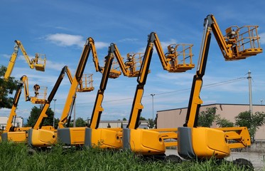Cherry pickers lined up in a parking lot with vertical hydraulic booms pointed to the sky. Side...