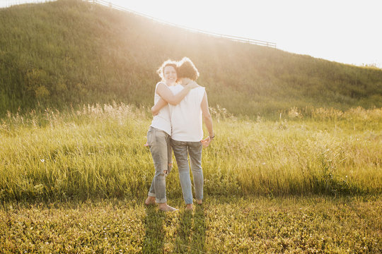 Two beautiful young women sisters in the same clothes walking around embracing on beautiful scenery country glade