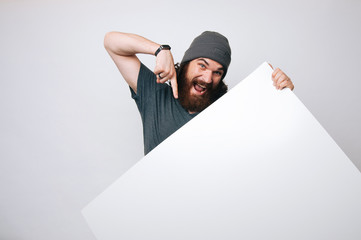 Young happy man looking at the camera hiding behind white sheet  for text. Blank sheet. Offer...