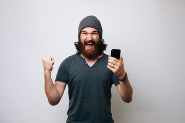 Cheerful young bearded man wearing grey T-shirt and fur cap hat is surprised and happy. Winner man...