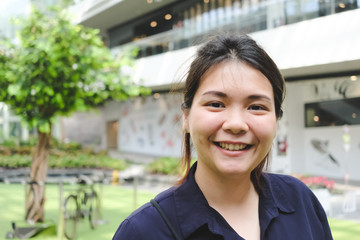 Close up of Asian woman smiling with building and tree background.