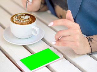 Mockup image of white mobile phone with green screen and hand holding phone. coffee on the table.