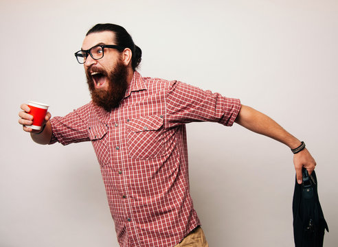 Young Bearded Man Running Wearing Glasses, Is Late To Work, Coffee To Go. Young Man Scared To Be Late, In A Hurry Or Rush. Rush Hour Concept.