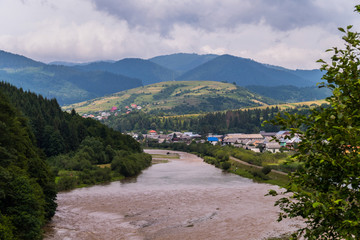 mountain landscape, panorama of a mountain river, village, green meadows and slopes against a...