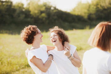 Positive laughing young female sisters in white t-shirts hug during a walk outside the city with family