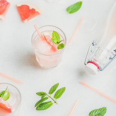 Flat-lay of cold refreshing summer alcohol cocktail with fresh grapefruit, mint and ice over white marble background, selective focus, square crop