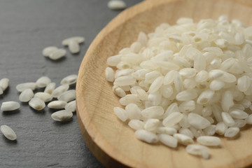 Arroz blanco redondo en una cuchara de madera sobre un fondo negro de piedra, detalle o macro