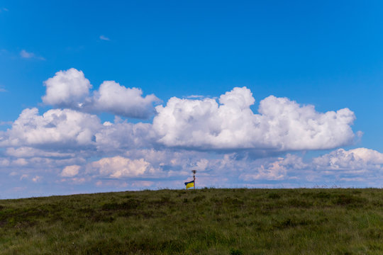 yellow-blue Ukrainian flag spreading by the wind on the top of a green mountain under the clouds