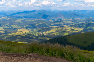 A magnificent landscape from the top of the mountain to other mountains and hills is covered with forest plantations and green grass over which the white clouds spill over