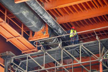 Workers welding work on district heating pipes under metal bridge